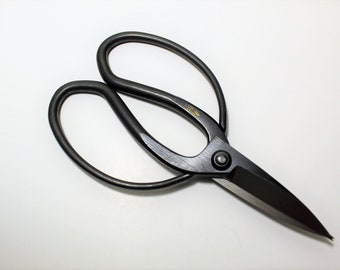 May include: Black metal pruning shears with a curved handle and a sharp blade. The shears have a gold inscription that reads "S.T.K.G."