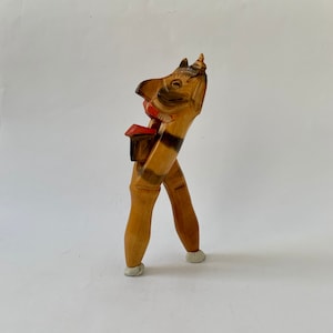 Op de afbeelding: Een houten notenkraker gebeeldhouwd in de vorm van een grillig figuur met een rode mond, zwarte ogen en een gestreept lichaam. De notenkraker heeft twee benen en een puntige hoed.