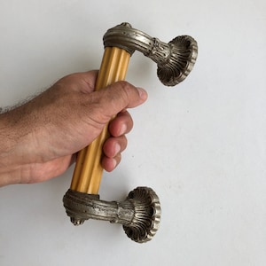 Könnte beinhalten: Ein antiker Türgriff mit einem gelben Kunststoffgriff und silbernen Metallakzenten. Der Griff hat ein dekoratives Design an den Enden.