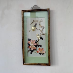 May include: A framed artwork featuring two gold-colored birds perched on branches with delicate blossoms. The artwork is encased in a wooden frame with a light green background, creating a serene and elegant aesthetic. The birds have black and gold details.