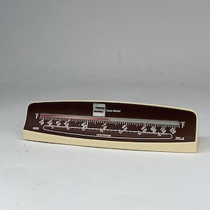 May include: A vintage Hertz Truck Rental thermometer with a brown and cream-colored casing. The thermometer displays Fahrenheit and Centigrade scales, with a temperature range from 20 to 120 degrees Fahrenheit. The text "Hertz Truck Rental" is visible.