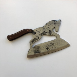 May include: A vintage metal cleaver with a wooden handle shaped like a running horse. The blade is dull and has a rustic patina.