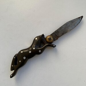 Puede incluir: Un cuchillo de bolsillo negro y blanco con manchas con un mango en forma de caballo. La hoja est&aacute; abierta y el mango est&aacute; hecho de un material oscuro con puntos blancos.