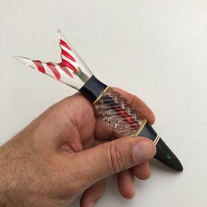 Könnte beinhalten: Ein roter und weiß gestreifter Glasfisch-Stift mit einem schwarzen und goldenen Griff und einem grünen Juwel am Ende.