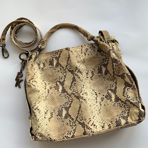 Può includere: Una borsa a mano in pelle di serpente beige con una tracolla in pelle marrone e un ciondolo dorato con le lettere "PK" su di esso.