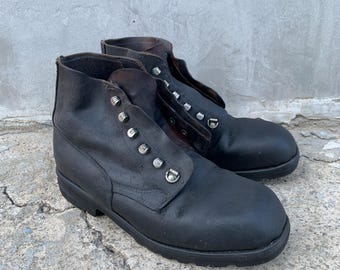 Op de afbeelding: Een paar zwarte leren enkellaarzen met een ronde neus, een dikke rubberen profielzool en een vetersluiting met zilverkleurige metalen oogjes en haken. De laarzen hebben een hoge schacht en een gladde, matte afwerking aan de buitenkant.