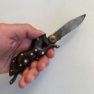 Puede incluir: Un cuchillo de bolsillo marr&oacute;n con un mango de caballo con lunares blancos. La hoja est&aacute; abierta y el cuchillo se sostiene en una mano.