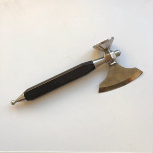 May include: A silver and black axe-shaped bottle opener with a black handle. The handle is a long, thin cylinder with a rounded end. The axe head is curved and has a small, round hole in the center.