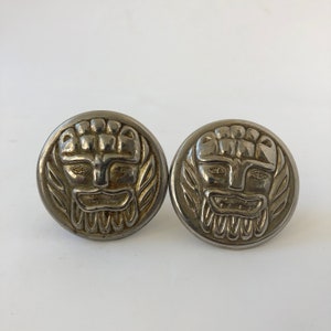 Könnte beinhalten: Zwei silberfarbene Manschettenknöpfe mit einem detaillierten Design eines Gesichts mit Bart und Krone. Die Manschettenknöpfe sind rund und haben eine glatte Oberfläche.