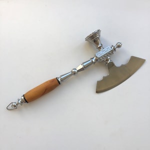 May include: A silver and wood meat cleaver with a decorative handle. The blade is curved and has a pointed tip. The handle is made of wood and has a decorative design.