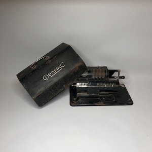 Puede incluir: Una máquina de sumar de metal negro con una cara plateada y una caja de transporte negra. La caja tiene la palabra "Феликс" escrita en blanco.