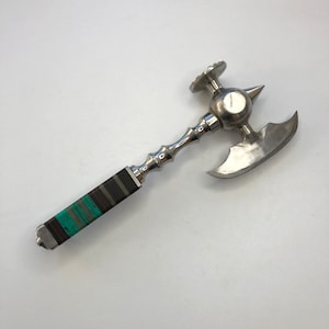 May include: A silver meat tenderizer with a black and green handle. The tenderizer has a spiked head and a blade.