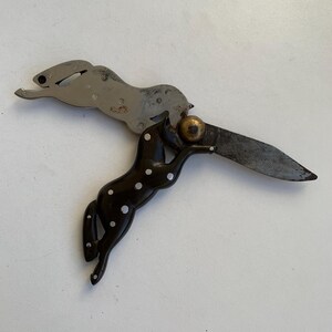 Puede incluir: Un cuchillo de bolsillo de plata con un dise&ntilde;o de caballo manchado de blanco y negro en el mango. La hoja est&aacute; abierta y el caballo sostiene una peque&ntilde;a bola dorada en la boca.