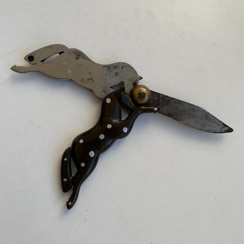 Puede incluir: Un cuchillo de bolsillo de plata con un dise&ntilde;o de caballo manchado de blanco y negro en el mango. La hoja est&aacute; abierta y el caballo sostiene una peque&ntilde;a bola dorada en la boca.