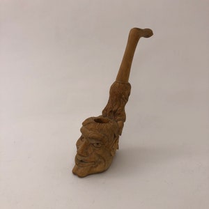May include: A wooden pipe carved in the shape of a man's head. The pipe is brown and has a long stem.