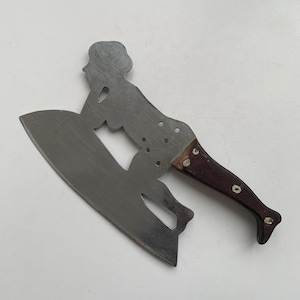 May include: A stainless steel cleaver with a dark brown wooden handle. The blade is shaped like a woman on a surfboard. The handle is attached with rivets.