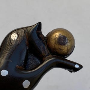 Puede incluir: Una figurita de madera negra y blanca con manchas de un perro sosteniendo una bola dorada en su boca.