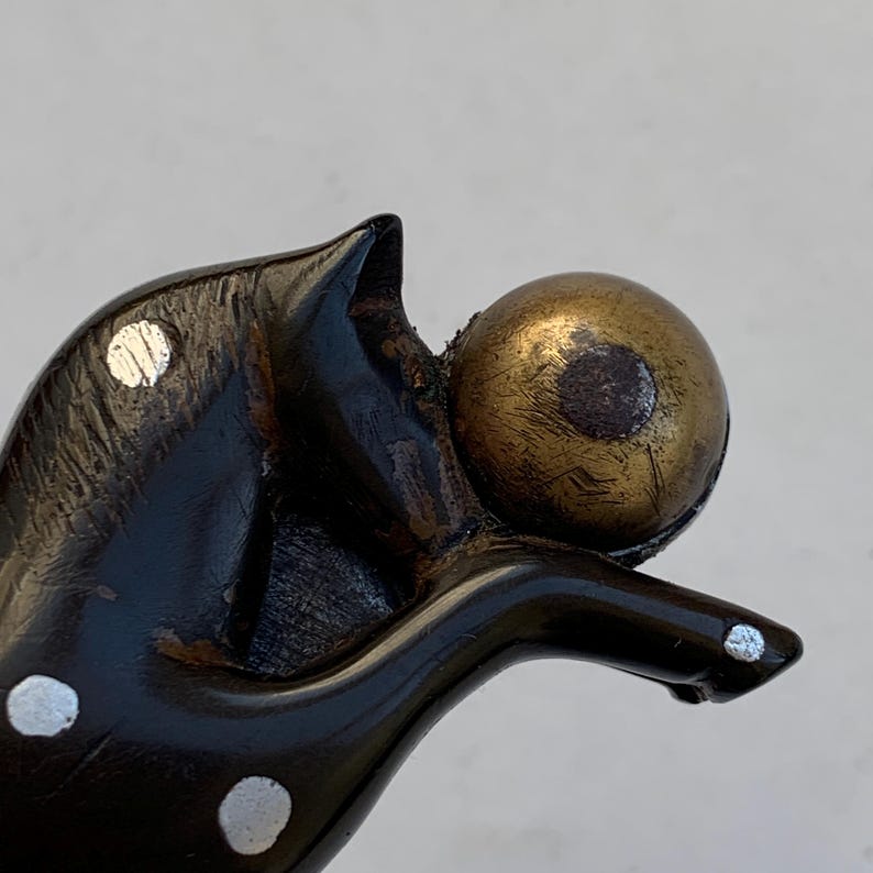 Puede incluir: Una figurita de madera negra y blanca con manchas de un perro sosteniendo una bola dorada en su boca.