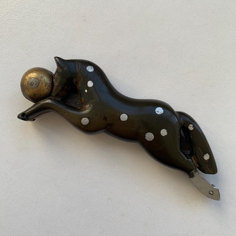 Puede incluir: Una figurita de caballo de madera negra y blanca con manchas blancas y una bola dorada en la boca. El caballo est&aacute; en una pose de carrera con la cola levantada.