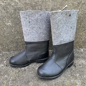 Puede incluir: Un par de botas tradicionales de fieltro. Las botas tienen un pie de cuero negro y una parte superior de fieltro gris. La parte superior de fieltro tiene motas de color. Botas diseñadas para climas fríos.