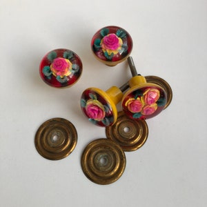 May include: Four vintage floral cabinet knobs with yellow and red glass and brass bases. The knobs feature pink and yellow roses with green leaves.