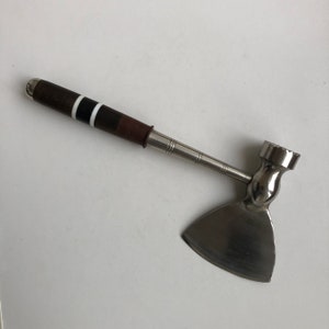 May include: A silver meat mallet with a brown handle and black accents. The mallet has a flat, wide head with a textured surface.