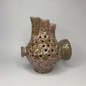 May include: A ceramic vase with a pink and green marbled glaze. The vase has multiple openings for flowers and a unique, asymmetrical shape.