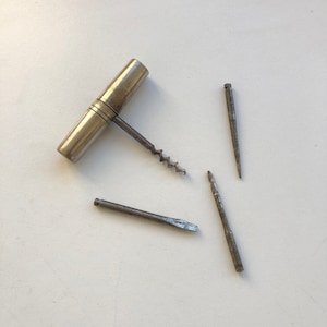 Peut inclure: Un outil multifonction en argent avec un tire-bouchon, un petit tournevis et deux poinçons. Les outils sont fixés à un manche en argent.