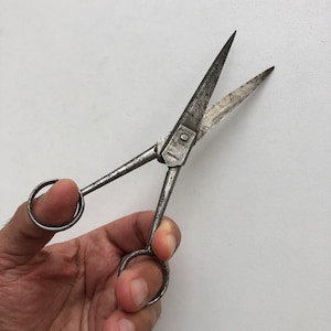 Peut inclure: Une paire de ciseaux en argent antique avec une seule poignée en anneau. Les ciseaux sont ouverts et tenus dans une main.