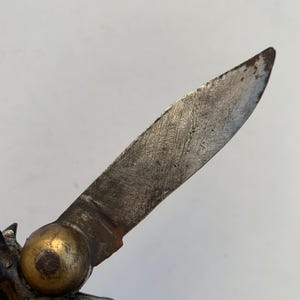 Puede incluir: Primer plano de una navaja de bolsillo vintage con mango de lat&oacute;n y una hoja parcialmente abierta. La hoja es de metal y tiene un aspecto desgastado y envejecido.