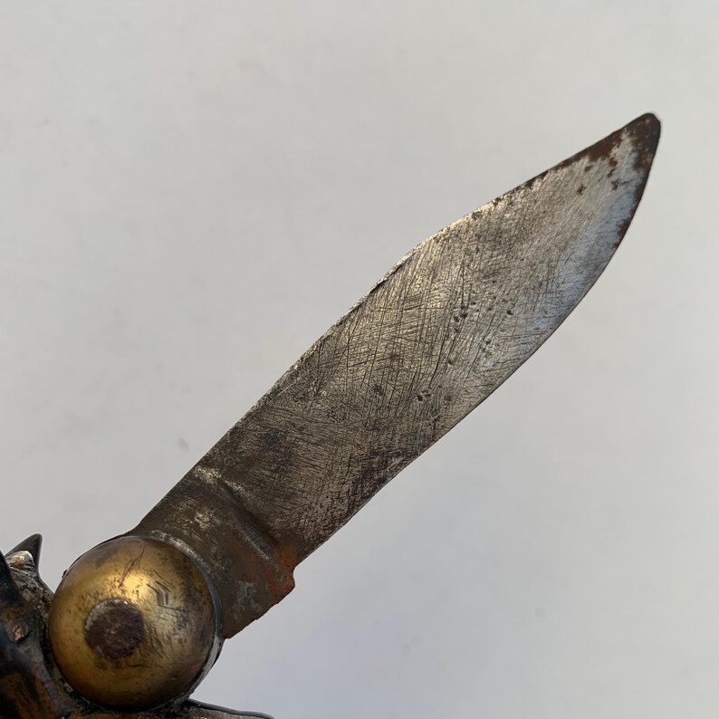 Puede incluir: Primer plano de una navaja de bolsillo vintage con mango de lat&oacute;n y una hoja parcialmente abierta. La hoja es de metal y tiene un aspecto desgastado y envejecido.