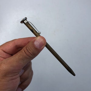 Puede incluir: Un manómetro de presión de neumáticos de latón con un clip plateado y una punta puntiaguda.