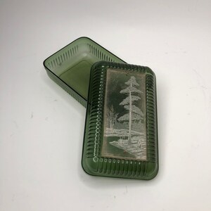 Peut inclure: Une boîte en verre vert avec un couvercle. Le couvercle présente un motif gravé blanc d'un pin et d'un paysage enneigé.