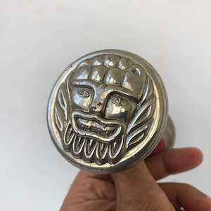 May include: Silver door knob featuring a detailed face design. The face has a wide mouth, large eyes, and a beard.