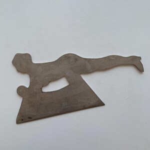 May include: A metal sculpture depicting a person in a diving pose. The sculpture is a flat, cutout design with a triangular base and a figure extending an arm. The metal has a brushed, silver finish.