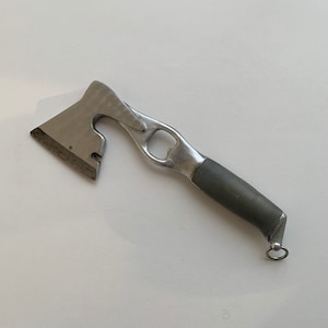 Könnte beinhalten: Eine silberne Axt mit einem Flaschenöffner und einem grauen Gummigriff. Die Axt hat einen kleinen Ring am Ende des Griffs.