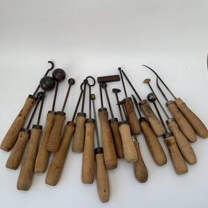 Könnte beinhalten: Eine Sammlung verschiedener Metall-Bildhauer- und Modellierwerkzeuge mit Holzgriffen. Das Set enthält Werkzeuge mit kugelförmigen, hakenförmigen, spitzen und flachen Enden sowie einen kleinen rechteckigen Block, alle mit verwitterten Holzgriffen.
