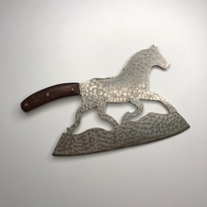 May include: A silver cleaver with a wooden handle. The blade is shaped like a horse running. The blade has a hammered texture.