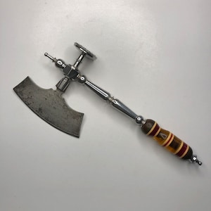 May include: A silver and wood meat cleaver with a serrated blade and a wooden handle with red and yellow stripes.