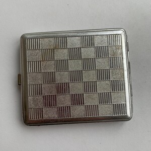 May include: A silver metal cigarette case with a chequered pattern.