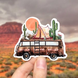 May include: A vintage camper van with a red and white striped tent on the roof, surrounded by cacti and a desert landscape. The van has a wooden ladder on the side and a brown and white patterned design.