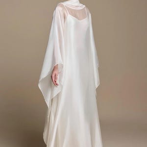 May include: A floor-length white gown featuring a sleeveless slip dress base and a sheer, flowing overlay with wide, cape-like sleeves and a high neckline. Text on the image lists model measurements: Height 165 cm, Bust 82 cm, Waist 64 cm, Hip 88 cm, Wear Size S.