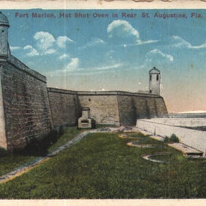May include: Vintage postcard depicting Fort Marion in St. Augustine, Florida. The image shows a stone fort with turrets under a blue sky with clouds. The text "Fort Marion, Hot Shot Oven In Rear St. Augustine, Fla." is visible.
