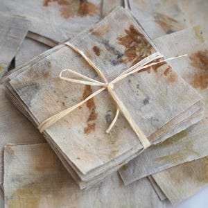 Peut inclure: Une pile de serviettes en lin carrées présentant des impressions botaniques dans des tons de brun, de beige et de vert sourd. Les serviettes sont attachées ensemble avec une fine ficelle de raphia clair, révélant des motifs de feuilles.