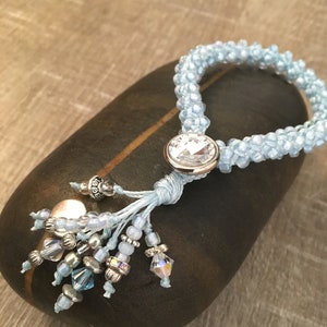 May include: A light blue beaded bracelet with a crystal charm and a silver bead. The bracelet has a tassel with silver and blue beads.
