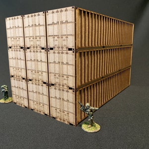 May include: A model of stacked wooden shipping containers, ideal for a tabletop game. The containers are light brown with detailed paneling. Two miniature figures are positioned nearby, adding to the scene.