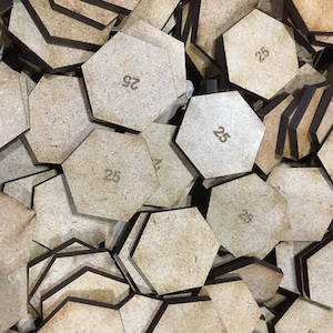 May include: A pile of brown hexagonal wooden game pieces with black edges. Each piece has the number "25" printed on it.