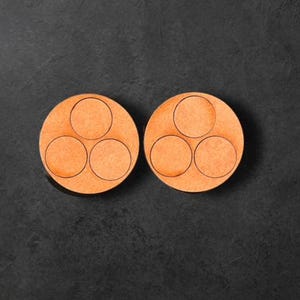 Puede incluir: Dos posavasos de madera con tres recortes circulares. Los posavasos son de color naranja claro.