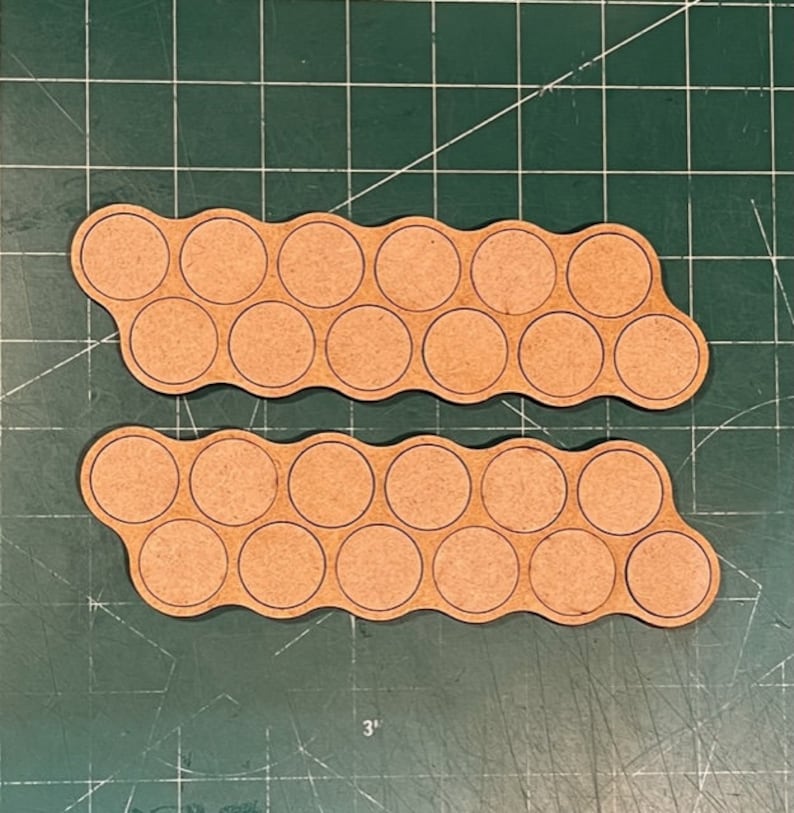 May include: Two wooden paint pot holders with 18 circular indentations for holding paint pots. The holders are made of light brown wood and have a wavy shape.