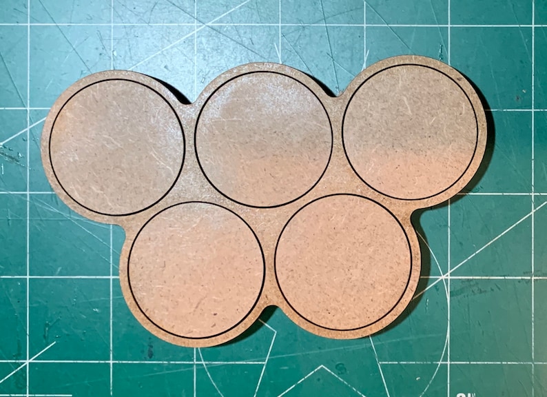 May include: A wooden paint pot holder with six circular compartments. The holder is brown and has a natural wood finish.